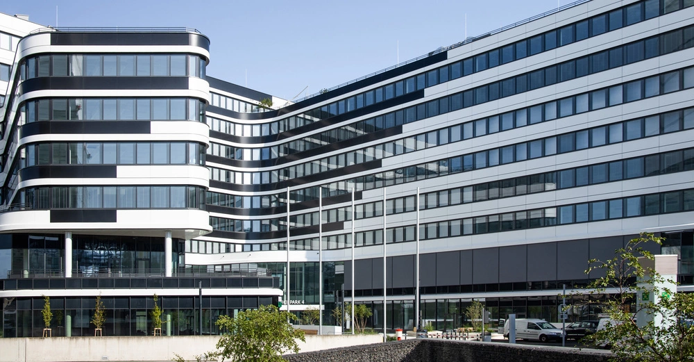 Gebäude mit moderner Architektur zeigt abgerundete Ecken und überwiegend Glasfassade mit schwarzen und weißen Streifen im urbanen Geschäftsumfeld. Text auf dem Gebäude lautet Green Park 4.