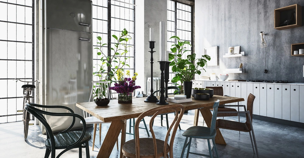 Großer Kühlschrank in moderner, industrieller Küche steht, umgeben von einem hölzernen Esstisch mit Stühlen und Pflanzen; hohe Fenster lassen viel Licht hinein