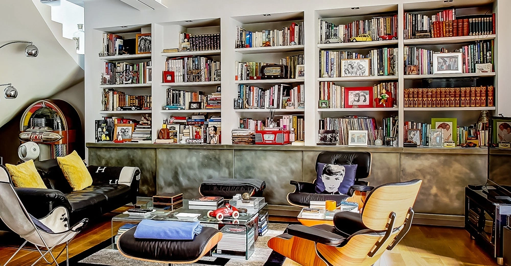 Bücherregale voller Bücher und Dekorationen füllen eine Wand eines modernen Wohnzimmers mit einem schwarzen Sofa einem Tisch mit Büchern und einem Jukebox im Hintergrund.