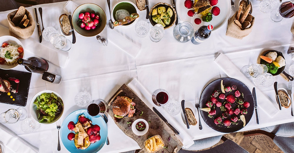 Eine weiße Leinentischdecke, gedeckt mit mehreren Tellern, Gläsern und einer Vielfalt an Gourmetgerichten.