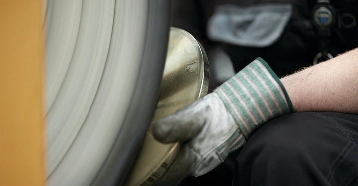 Person trägt Handschuhe arbeitet an einem rotierenden Schleifrad poliert eine Metallplatte Arbeitsplatz im Hintergrund unscharf