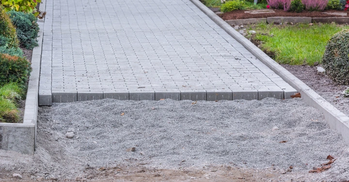 Gepflasterter Gehweg wird gebaut und endet abrupt in einem Gartenbereich mit Büschen und Gras im Hintergrund