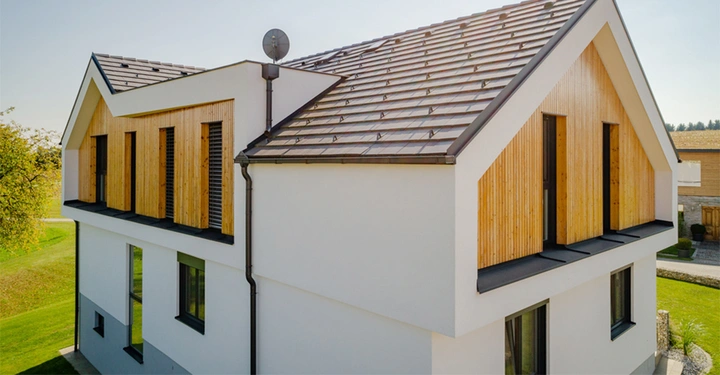 Modernes zweistöckiges Haus mit Satteldach und weißen Wänden Fenster mit Holzverkleidung Terrasse und Sat-Schüssel Garten und Nachbarhäuser im Hintergrund helle Tageslichtbedingungen.
