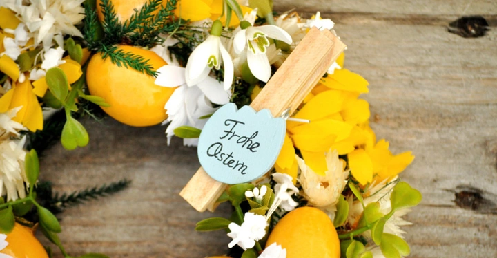 schön geschmückter Oster-Türkranz mit gelben Eiern, Osterglocken und Narzissen sowie einem kleinen Schild mit der Aufschrift Frohe Ostern.
