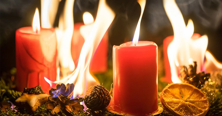Adventskranz mit vier lichterloh brennenden roten Kerzen, die eine hohe Brandgefahr zur Weihnachtszeit darstellen.
