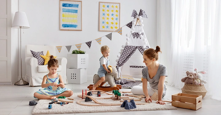 Beispiel für gelungene Kinderzimmer-Raumplanung: Eine Mutter spielt mit ihren Kindern in einem hellen, organisierten Raum mit Spielzelt, cleveren Aufbewahrungslösungen und einer gemütlichen Spielecke auf dem Teppich.