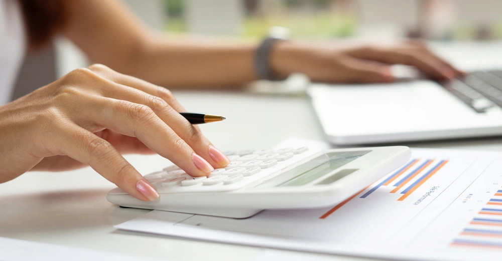 Frauenhände an Schreibtisch mit Taschenrechner und Planer und Kugelschreiber brüten über Rechnungen