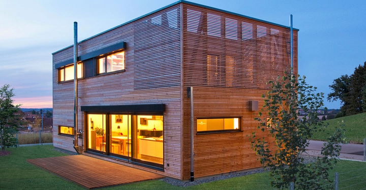 Holzhaus scheint im Innenbereich beleuchtet auf offener Wiese bei Sonnenuntergang