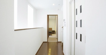 Aufzugstür ist geschlossen im Flur mit Holzfußboden und weißen Wänden zu sehen und endet in einem offenen Durchgang, der zu einem möblierten Raum führt