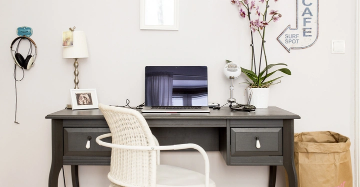 Galerie-Bild 8: Ein schwarzer Schreibtisch mit einem Laptop darauf, umgeben von einer Lampe, einem eingerahmten Bild, einer Pflanze und einem Mikrofon; im Hintergrund hängt ein Schild mit der Aufschrift CAFE SURF SPOT.