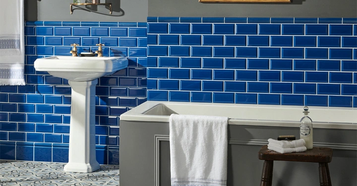 Waschbecken steht auf einem Sockel mit zwei Wasserhähnen blauer Kachelrückwand und Wandhandtüchern Badezimmer Context eine Badewanne mit Handtuch darauf daneben ein Hocker mit Seife und Flasche.