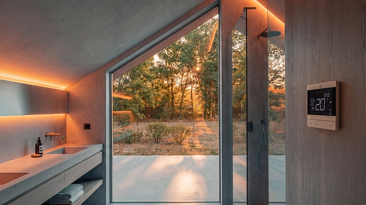 Galerie-Bild 3: Modernes Badezimmer mit Sichtbetonwänden, im Vordergrund ein Wandpaneel, das die Raumtemperatur anzeigt.