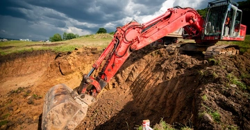 roter Bagger beim Ausheben einer Baugrube, im Hintergrund bedrohlich wirkender Gewitterhimmel, Foto sehr verzerrt, perspektivisch aufgenommen