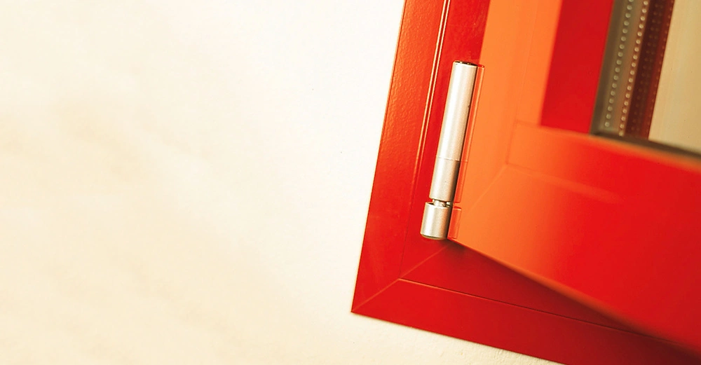 Roter Fensterrahmen öffnet sich gerade an einer silbernen Scharnierseite gegen eine cremefarbene Wand.