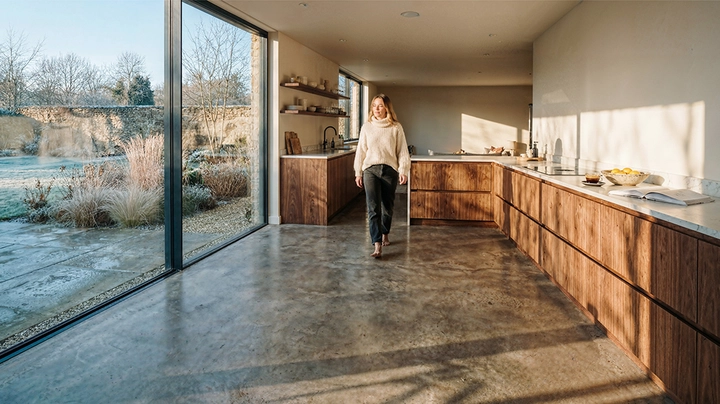 Galerie-Bild 2: Frau geht durch großzügige Küche, Winterlandschaft draußen, Sonne strahlt herein, Frau ist in Winterklamotten aber Barfuß