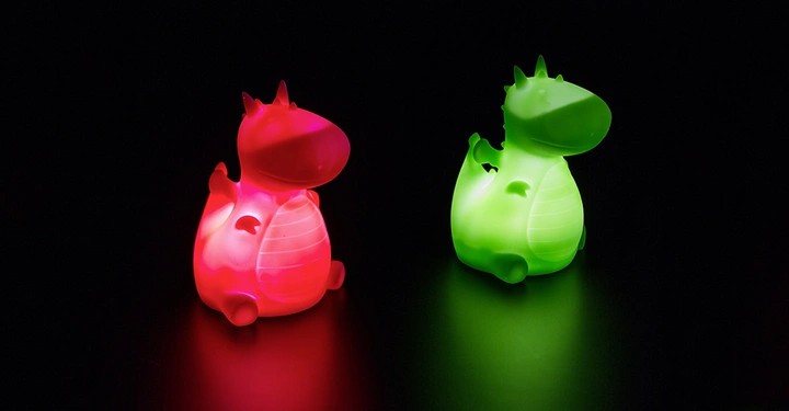 Galerie-Bild 6: Zwei kleine, leuchtende Drachenfiguren sitzen nebeneinander im Dunkeln. Eine ist rot und die andere ist grün. Die Drachen haben hervorstehende Bäuche und kleine Hörner auf den Köpfen.