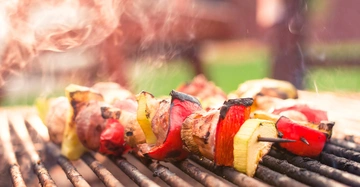 Gemüsespieße braten auf einem Grill im Freien in einem grünen Park mit rauchiger Atmosphäre.