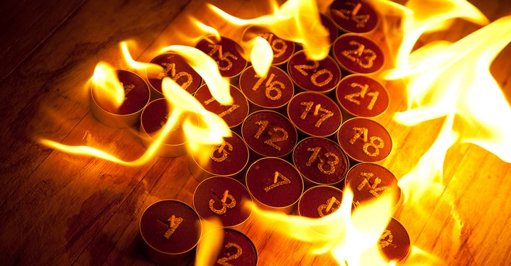 Adventskalender aus nummerierten Teelichtern, deren Flammen gefährlich ineinander übergehen und einen Hitzestau auf dem Holztisch verursachen.