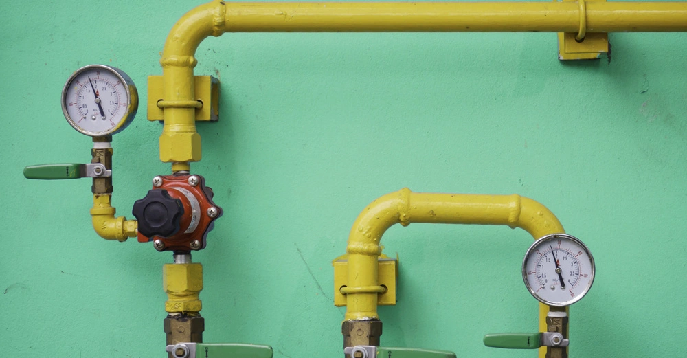 Gelbe Rohre und Druckanzeigen sind verbunden und verlaufen entlang einer grünen Wand Die Rohre haben Ventile mit grünen Griffen und Messuhren zeigen Druckwerte an