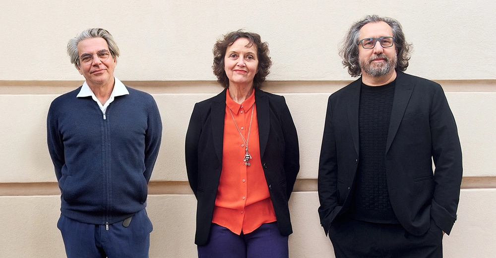 Portrait der Kurator:innen Lorenzo Romito, Sabine Pollak und Michael Obrist vor einer beigen Wand.