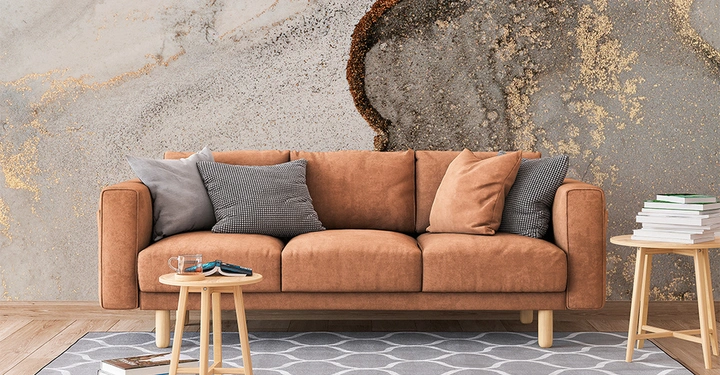 Galerie-Bild 4: Braunes Sofa steht vor einer künstlerisch gestalteten Wand im Muster eines Marmors. Kissen liegen auf dem Sofa. Ein kleiner runder Holztisch mit Büchern und einem Glas steht davor.
