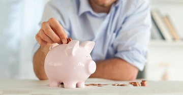 Rosa Sparschwein auf Tisch Mann steckt Münze hinein Im Hintergrund Bücherregal