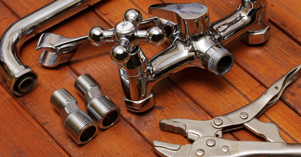 Metallhahn ist nicht montiert und liegt neben zwei Verschraubungen und einer Zange auf einem hölzernen Untergrund.