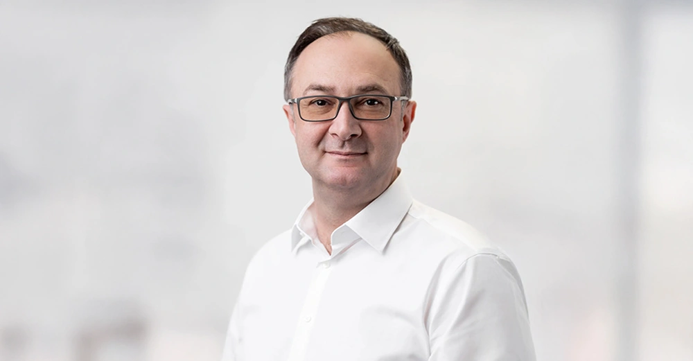 Alen Music, neuer Geschäftsführer von immOH! steht mit weißem Hemd und freundlich lächelnd vor weißem Hintergrund. 