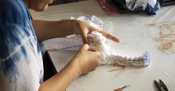 Person näht einen Stoff an einem Tisch in einem hellen Raum