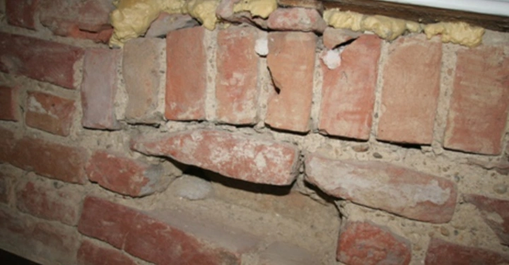 Galerie-Bild 25: Ziegelwand zeigt beschädigte bzw. fehlende Steine Lücken mit gelbem Isolierschaum umrandet. Die Umgebung ist ein Innenraum mit einem weißen Fensterrahmen am oberen Bildrand.