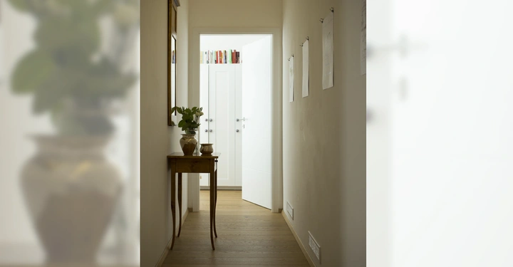 Galerie-Bild 7: Holztisch mit Pflanze steht in einem schmalen Flur neben einem Spiegel Zeichnungen an der Wand Tür am Ende des Flurs ist geöffnet Regal mit Büchern sichtbar