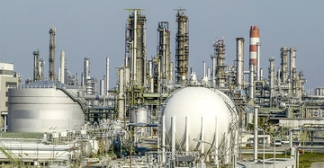 Industrieanlage mit mehreren Tanks und Türmen steht still umgeben von Pipelines und metallischen Strukturen unter klarem Himmel.