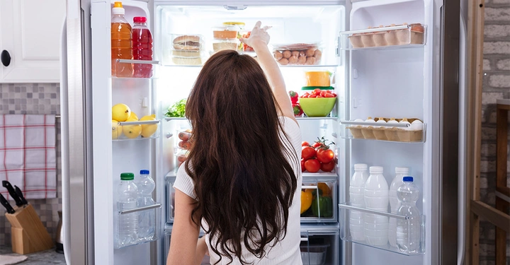 Frau öffnet einen gefüllten Kühlschrank in einer Küche und greift nach einem Lebensmittelregal.