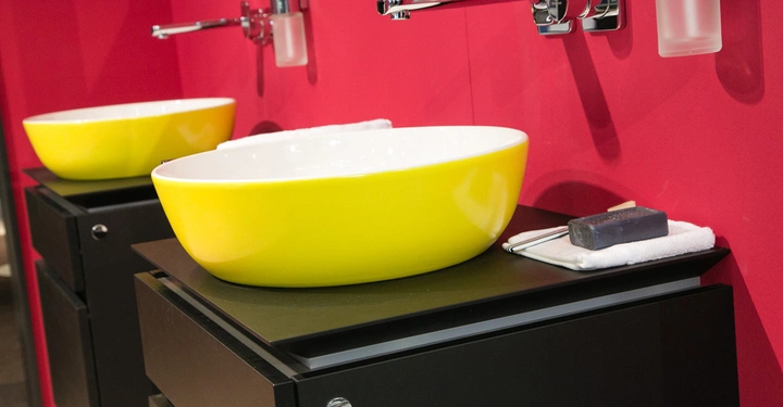 Galerie-Bild 3: Zwei gelbe Waschbecken auf schwarzen Schränken mit je einem Wasserhahn und einem Wandseifenspender vor einer rosa Wand.