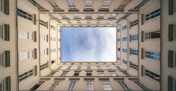 Rechteckiger Innenhof von unten betrachtet zeigt beige Gebäude mit vielen Fenstern und offenen Himmel in der Mitte.