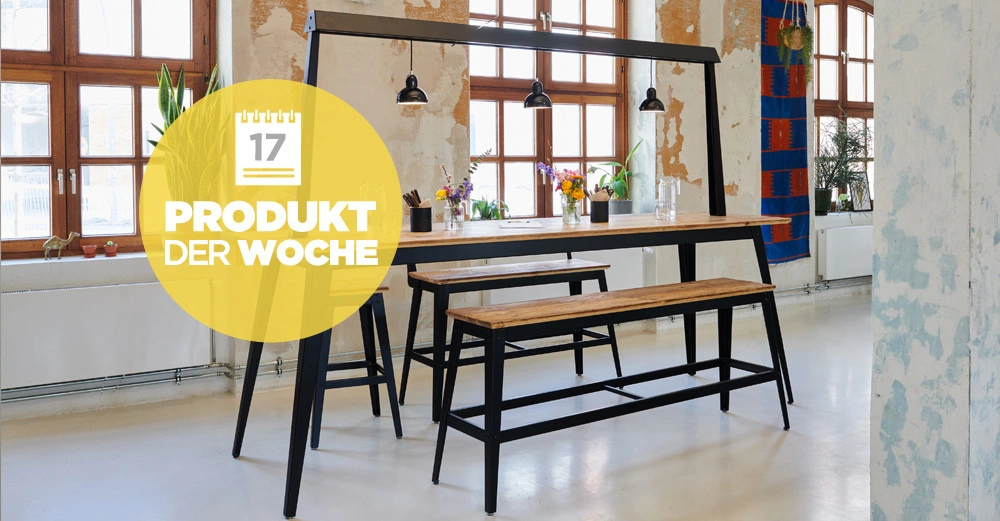 Holztisch mit zwei Bänken steht unter Hängelampen in einem Raum mit großen Fenstern und Pflanzen Text 17 PRODUKT DER WOCHE