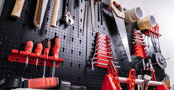 Werkzeuge hängen an einer schwarzen Lochwand festgehalten durch rote Halterungen die Schraubendreher Sägen Zangen und Klebeband in einer gut organisierten Werkstattumgebung arrangieren.