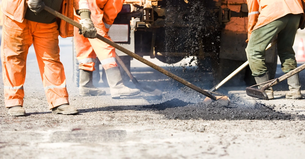 Bauarbeiter in Schutzkleidung teeren eine dampfende Straße