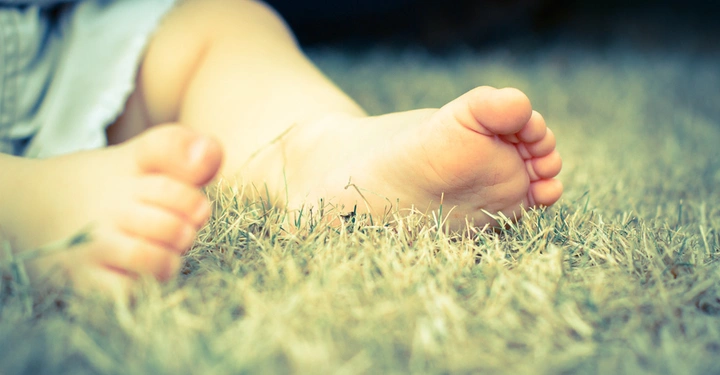 Babyfüße liegen ruhig auf trockenem Gras im Freien