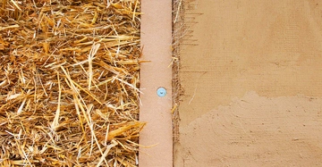 Eine Wand, zur Hälfte mit Stroh gefüllt, zur Hälfte bereits mit Lehm verputzt.