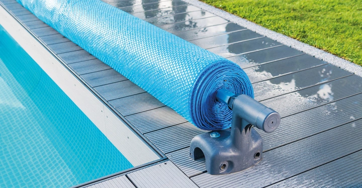 aufgerollte türkisblaue Luftpolsterfolie auf Rolle für Poolabdeckung. Teil des Swimmingpools zu sehen.