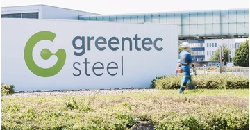 greentec steel Logo auf großer weißer Betonwand, vorne Rasen und Beete, ein Arbeiter geht vorbei