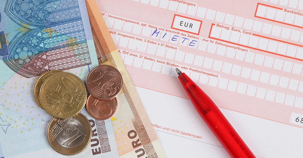 Erlagschein mit Wort Miete bei Verwendungszweck, Kugelschreiber rechts und Euroscheine und Münzen links