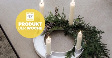 Adventskranz Winter Glow von Villeroy & Boch dekoriert mit vier brennenden weißen Kerzen und einem elegant drapierten Tannenzweig.
