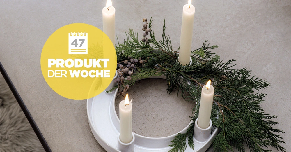 Adventskranz Winter Glow von Villeroy & Boch dekoriert mit vier brennenden weißen Kerzen und einem elegant drapierten Tannenzweig.