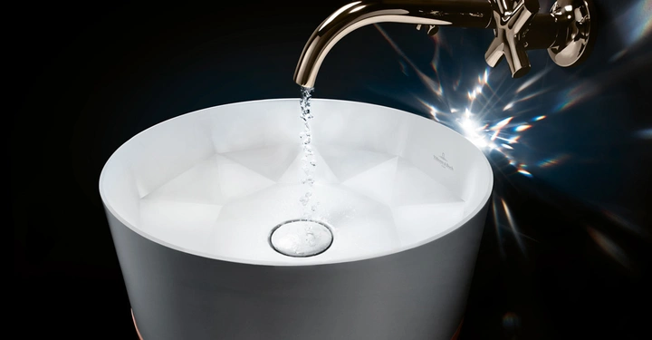 Ein weißes, modernes Waschbecken fängt Wasser, das aus einem glänzenden, metallischen Wasserhahn fließt Hintergrund ist dunkel.