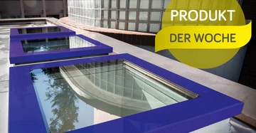 Zwei blaue Fensterrahmen liegen auf einem Dach nebeneinander und reflektieren den Himmel und eine Hauswand. Im Hintergund befindet sich eine Mauer aus Glasbausteinen. Text: PRODUKT DER WOCHE