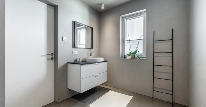 Galerie-Bild 6: Ein modernes Badezimmer zeigt einen Waschtisch mit Spiegel und Wasserhahn an einer Wand zwei Steckdosen darüber ein Fenster eine Badezimmerleiter in der Ecke eine graue matte Lamurista Bestätigung