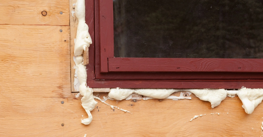 Fensterrahmen rot wurde mit beigem Dichtmittel umrandet auf Holzwand befestigt.