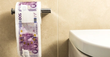 Toilettenpapier hängt an einer Wandhalterung und ist mit dem Motiv eines 500 Euro-Scheins bedruckt Kontext Badezimmer mit beigen Fliesen und einer weißen Toilettenschüssel